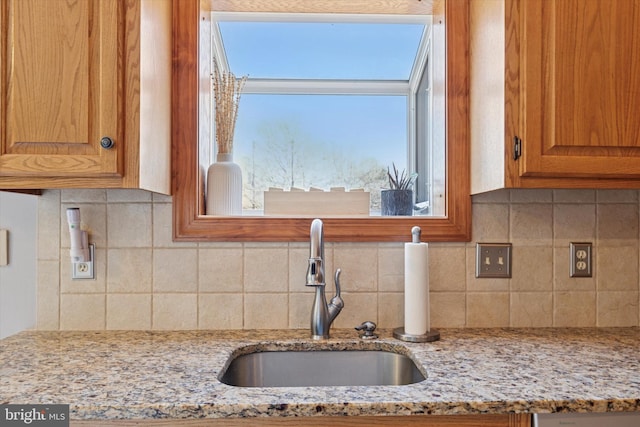 kitchen with a healthy amount of sunlight, tasteful backsplash, light stone counters, and a sink