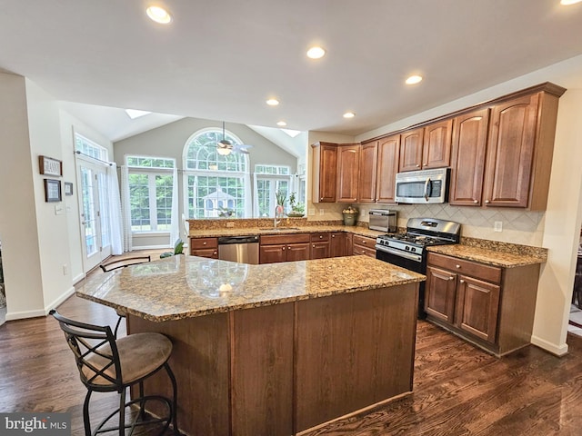 kitchen with dark wood finished floors, tasteful backsplash, appliances with stainless steel finishes, lofted ceiling with skylight, and light stone countertops