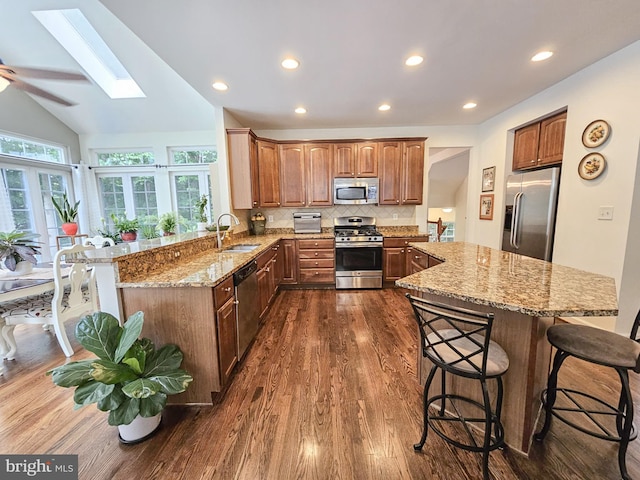 kitchen with stainless steel appliances, a sink, light stone counters, and a kitchen breakfast bar