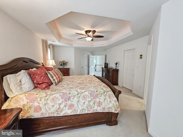 bedroom with light carpet, baseboards, a tray ceiling, and ceiling fan