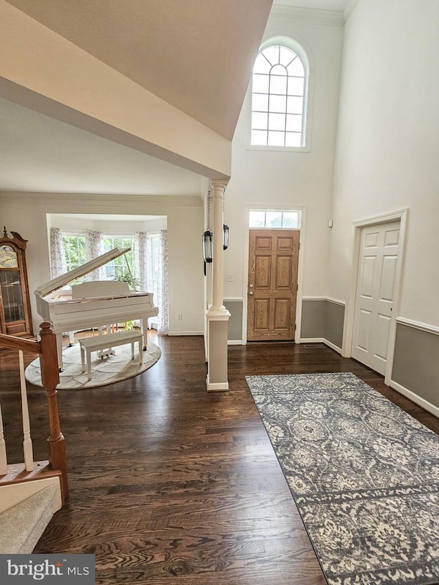 foyer entrance with dark wood-style flooring, a high ceiling, decorative columns, and baseboards