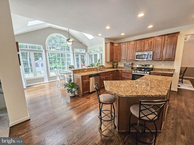 kitchen featuring vaulted ceiling with skylight, tasteful backsplash, light stone counters, a peninsula, and stainless steel appliances