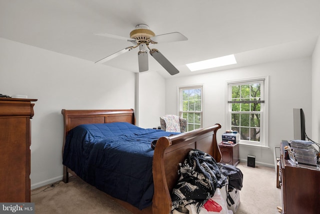 bedroom featuring light carpet, a skylight, baseboards, and ceiling fan