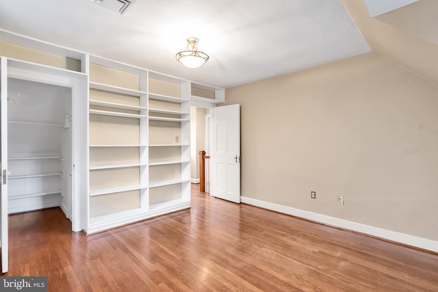 unfurnished bedroom with wood finished floors, visible vents, baseboards, a closet, and a walk in closet