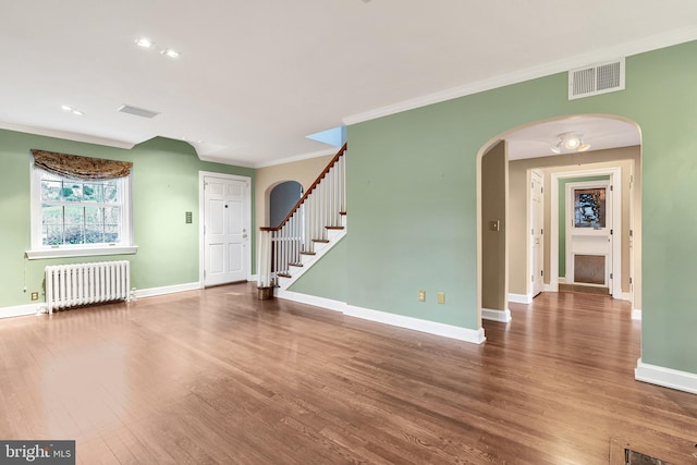 unfurnished living room featuring visible vents, wood finished floors, radiator heating unit, arched walkways, and crown molding