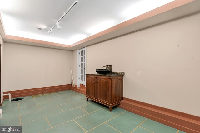 interior space featuring visible vents, baseboards, a tray ceiling, track lighting, and dark tile patterned floors