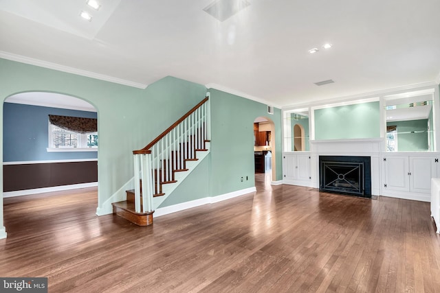 unfurnished living room featuring a fireplace with flush hearth, wood finished floors, stairway, arched walkways, and crown molding