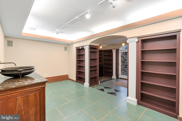 unfurnished office featuring baseboards, decorative columns, arched walkways, a sink, and rail lighting