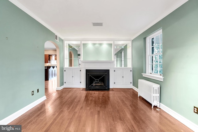 unfurnished living room featuring radiator, baseboards, a fireplace with flush hearth, wood finished floors, and arched walkways