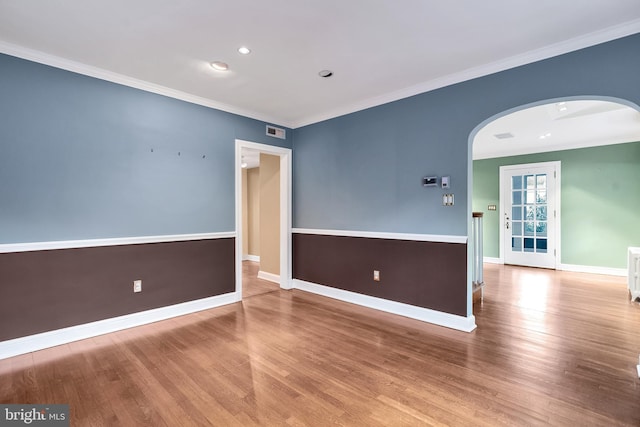 empty room with crown molding, wood finished floors, and arched walkways