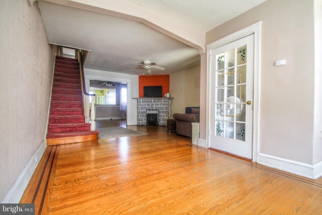 unfurnished living room featuring a ceiling fan, stairway, wood finished floors, and a stone fireplace