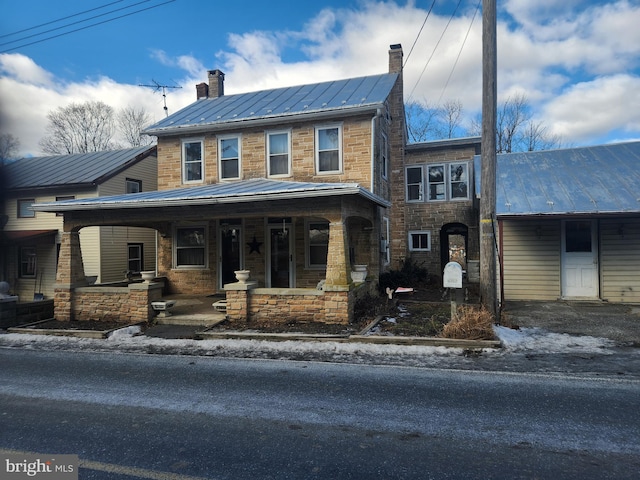 view of front of property featuring stone siding, covered porch, metal roof, and a chimney