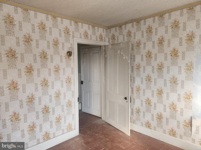 unfurnished room with crown molding, a textured ceiling, baseboards, and wallpapered walls