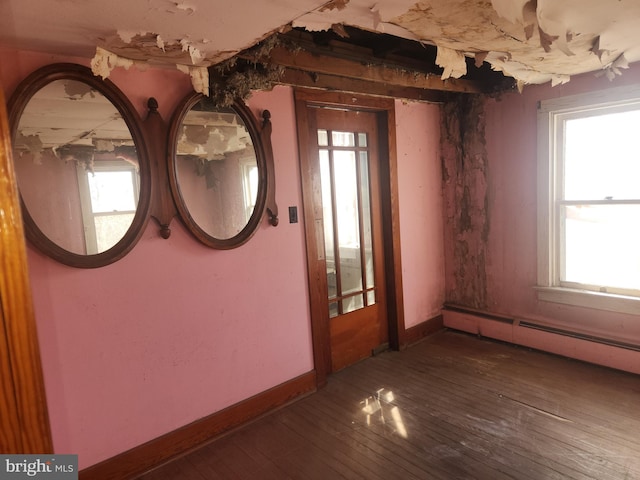 unfurnished room featuring a baseboard heating unit, hardwood / wood-style floors, and baseboards