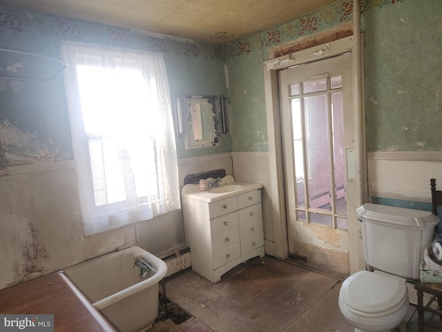 full bathroom with toilet, a wainscoted wall, a freestanding tub, and vanity