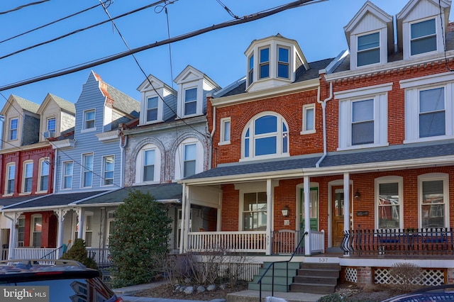 townhome / multi-family property featuring brick siding, a residential view, a porch, and a shingled roof