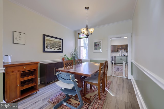 dining room with an inviting chandelier, crown molding, and light wood-style flooring