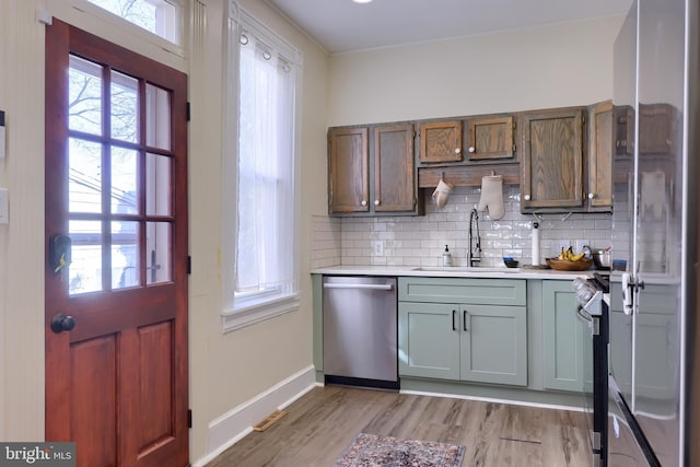 kitchen featuring a sink, backsplash, appliances with stainless steel finishes, light wood finished floors, and light countertops