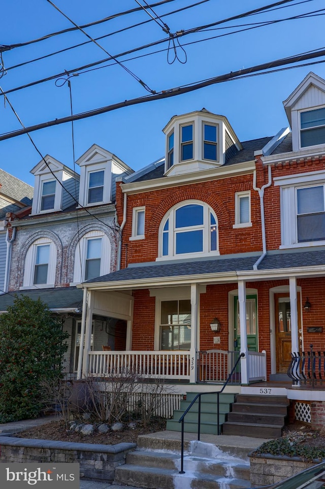 townhome / multi-family property with brick siding, covered porch, and a shingled roof