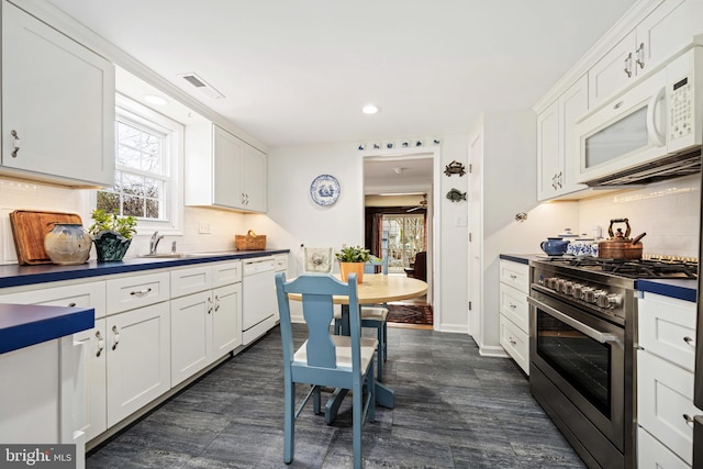 kitchen with dark countertops, white appliances, white cabinetry, and baseboards