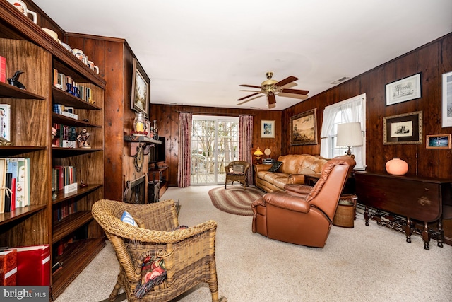 sitting room featuring visible vents, a ceiling fan, carpet, wood walls, and a fireplace