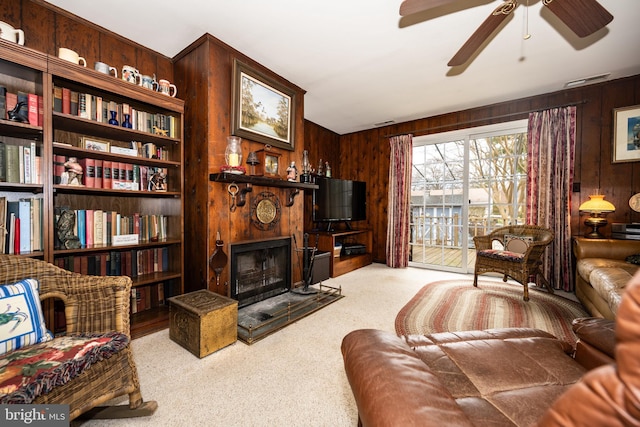 living room with ceiling fan, carpet floors, wood walls, and a fireplace