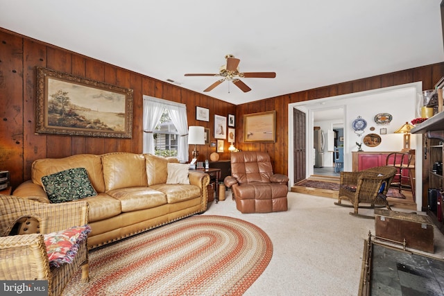 carpeted living area featuring wood walls, ceiling fan, a fireplace, and visible vents