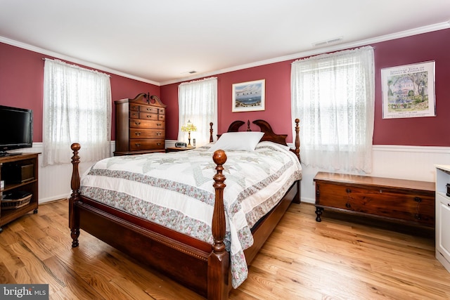 bedroom featuring ornamental molding, wainscoting, visible vents, and light wood-style floors