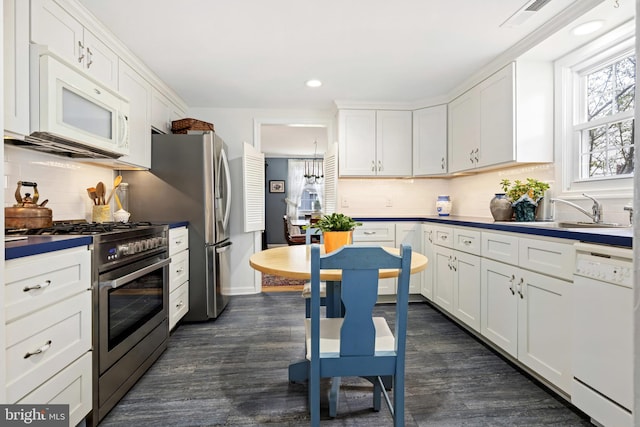 kitchen with dark wood finished floors, visible vents, white cabinets, a sink, and white appliances