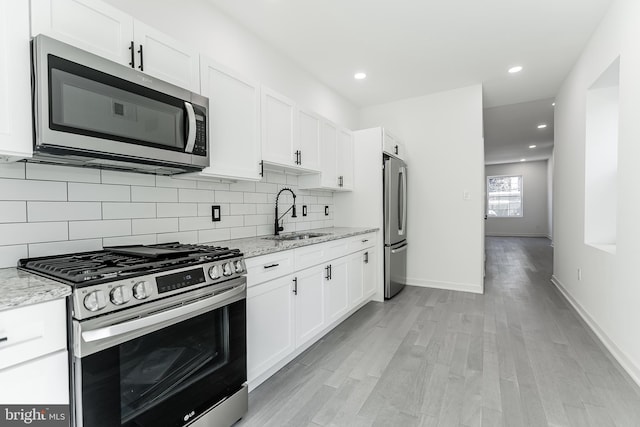 kitchen with stainless steel appliances, a sink, white cabinetry, and decorative backsplash