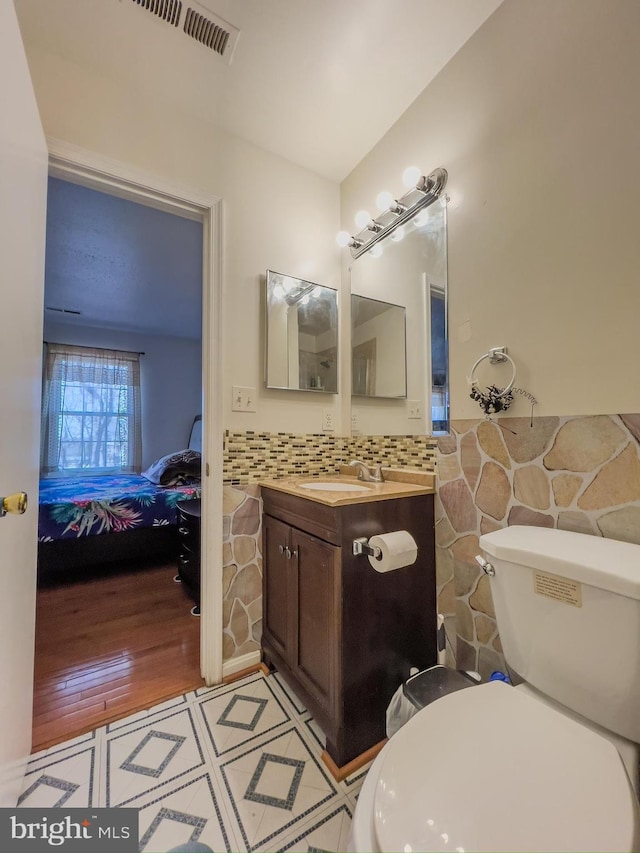 ensuite bathroom featuring a wainscoted wall, visible vents, toilet, ensuite bathroom, and vanity