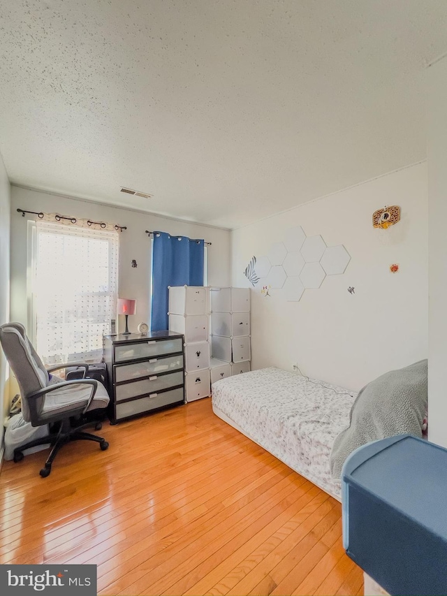 bedroom featuring hardwood / wood-style flooring, visible vents, and a textured ceiling