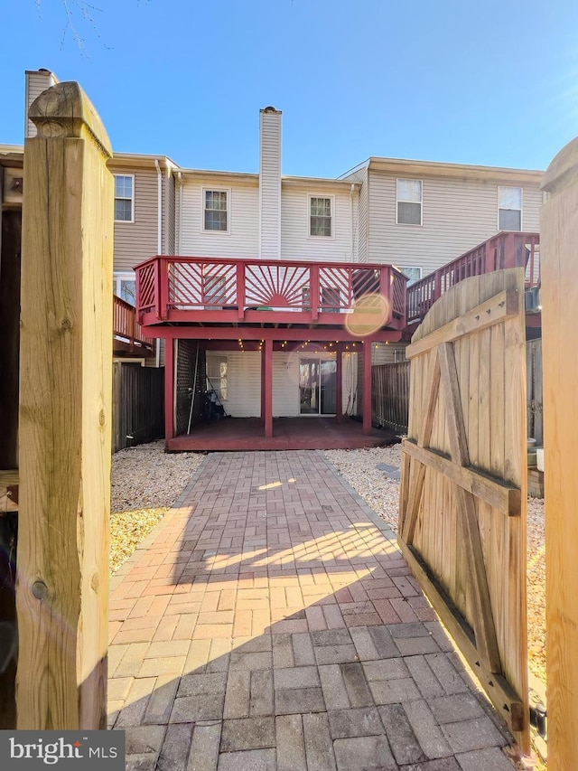 back of house with a chimney, fence, a deck, and a patio