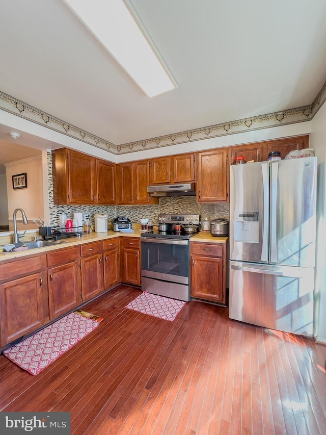 kitchen featuring under cabinet range hood, light countertops, appliances with stainless steel finishes, decorative backsplash, and dark wood finished floors