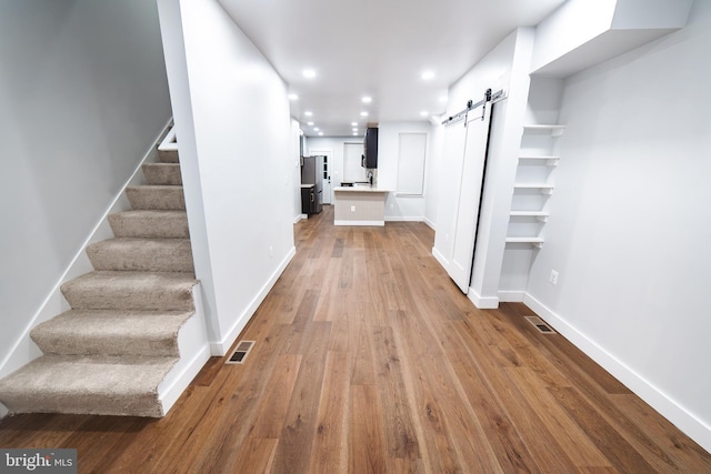 hallway featuring a barn door, visible vents, wood finished floors, stairs, and recessed lighting