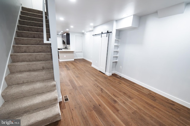 finished below grade area with visible vents, a barn door, wood finished floors, baseboards, and stairs