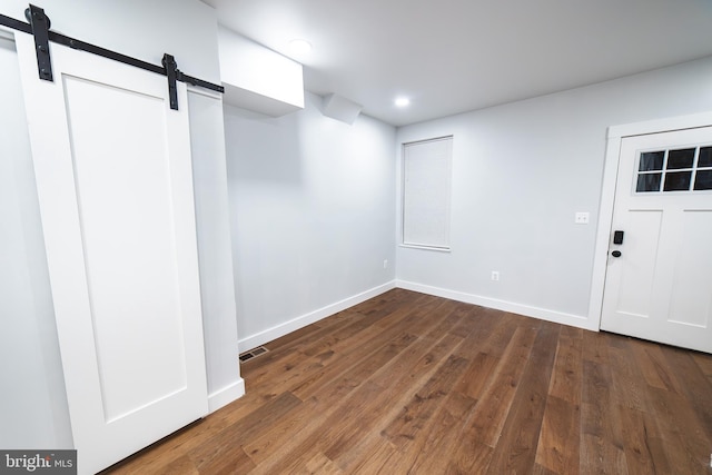 basement featuring a barn door, baseboards, visible vents, dark wood-style flooring, and recessed lighting