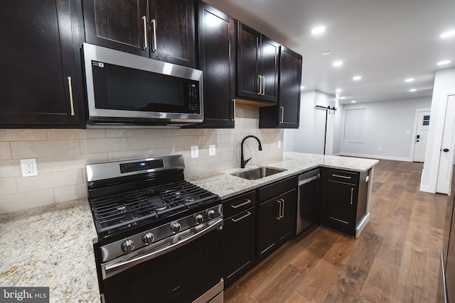 kitchen with a barn door, a peninsula, dark wood-style flooring, a sink, and appliances with stainless steel finishes