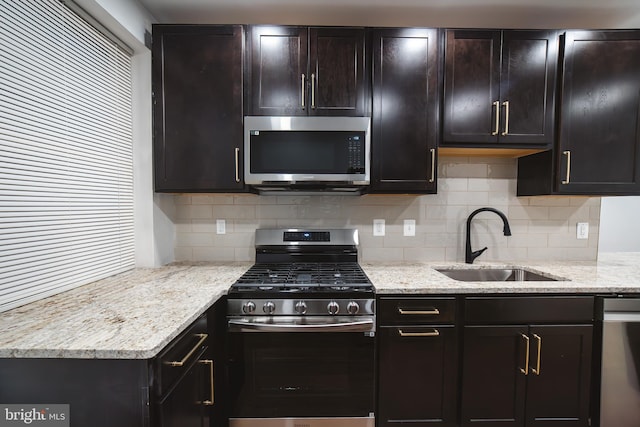 kitchen with stainless steel appliances, a sink, light stone counters, and decorative backsplash