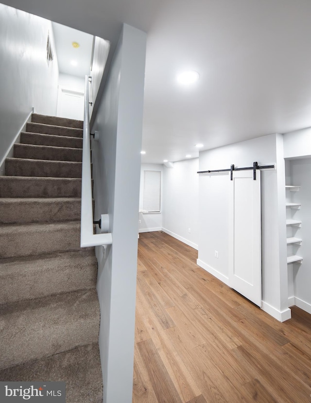 stairway with a barn door, baseboards, wood finished floors, and recessed lighting