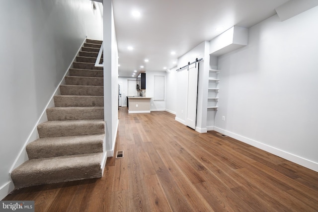 below grade area featuring a barn door, baseboards, visible vents, wood finished floors, and stairs