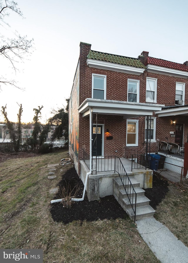 townhome / multi-family property featuring a tiled roof, brick siding, and a porch