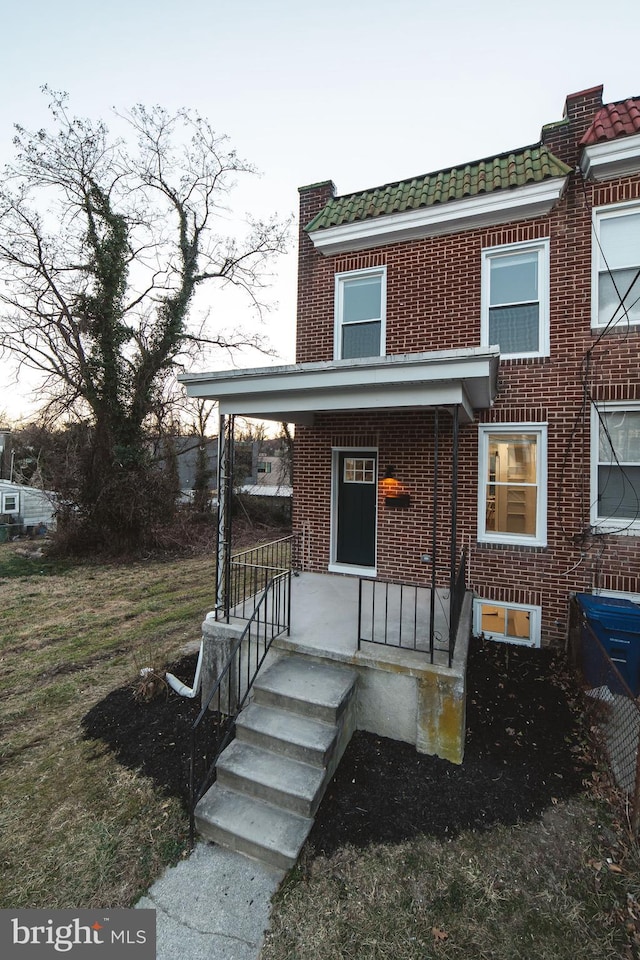 view of front facade with covered porch, brick siding, and mansard roof