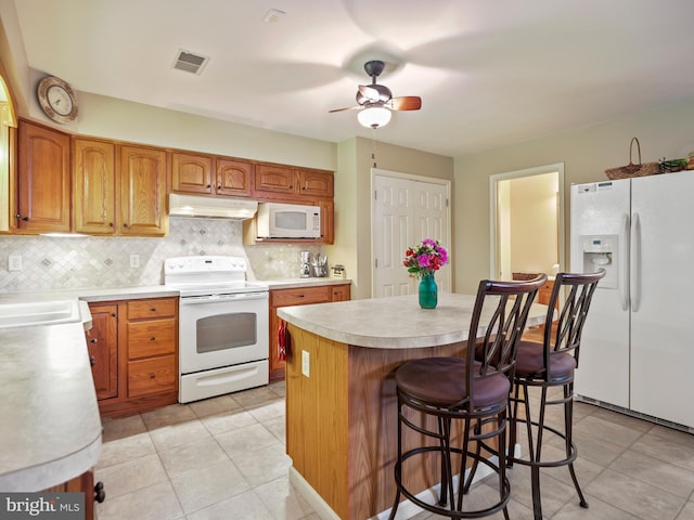 kitchen with white appliances, visible vents, decorative backsplash, light countertops, and under cabinet range hood