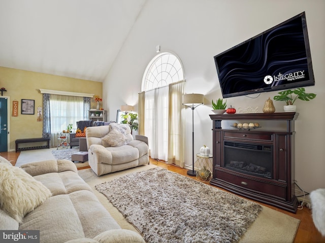 living area with high vaulted ceiling, a glass covered fireplace, and wood finished floors