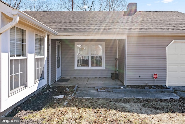 doorway to property featuring a garage, a patio, and roof with shingles