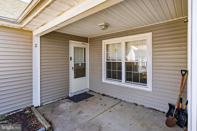 view of exterior entry featuring roof with shingles and a patio