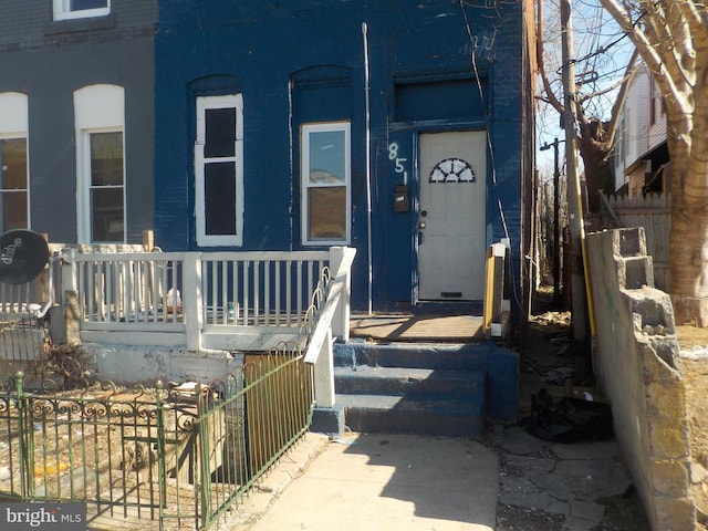 view of exterior entry with a porch, fence, and brick siding