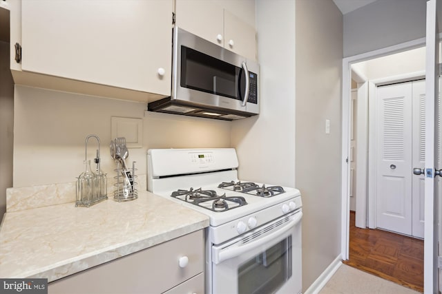 kitchen featuring light stone counters, baseboards, white cabinets, white range with gas cooktop, and stainless steel microwave