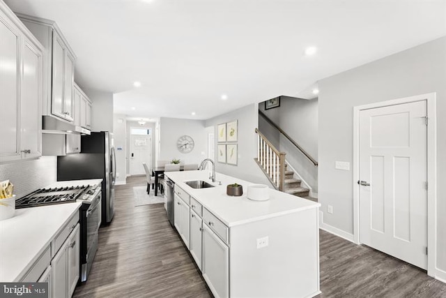 kitchen featuring a kitchen island with sink, stainless steel appliances, a sink, light countertops, and dark wood-style floors